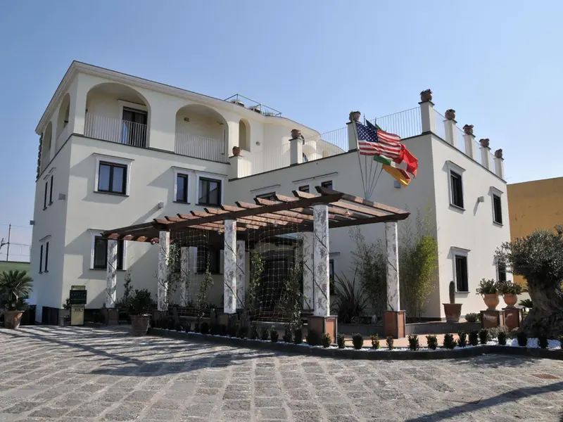 Bâtiment blanc à deux étages avec une pergola et des pots de fleurs.