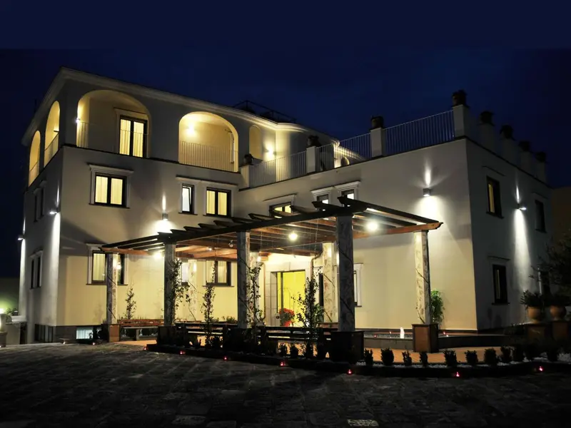 Bâtiment blanc éclairé avec une pergola et un jardin soigné.