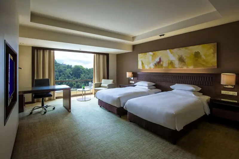 Une chambre d'hôtel lumineuse avec deux lits simples et une vue sur la végétation.