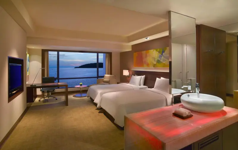 Chambre lumineuse avec deux lits simples et vue sur la mer.