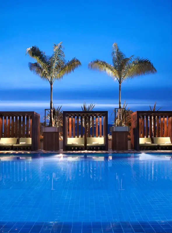 Trois lits de repos bordent une piscine illuminée sous un ciel bleu foncé.