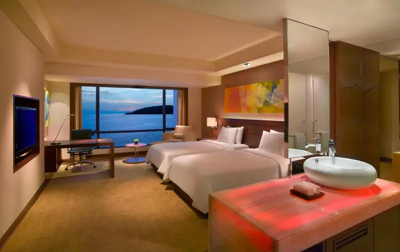 Chambre lumineuse avec deux lits simples et vue sur la mer.