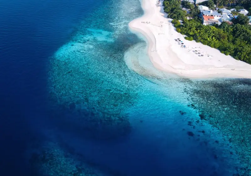 Vue aérienne d'une plage de sable blanc bordée d'eaux turquoise et d'un récif corallien.