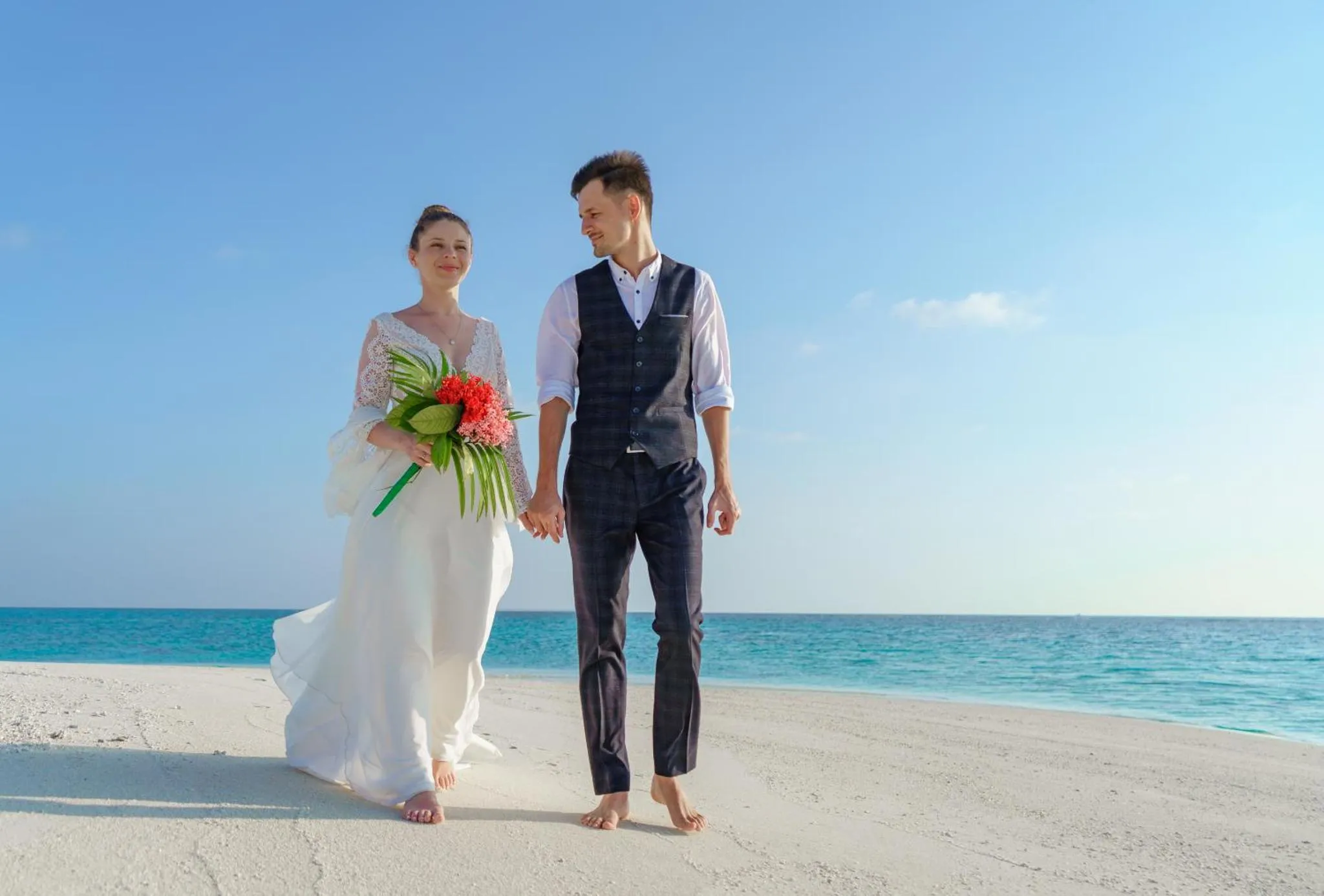 Un couple se promène sur une plage de sable blanc face à la mer.