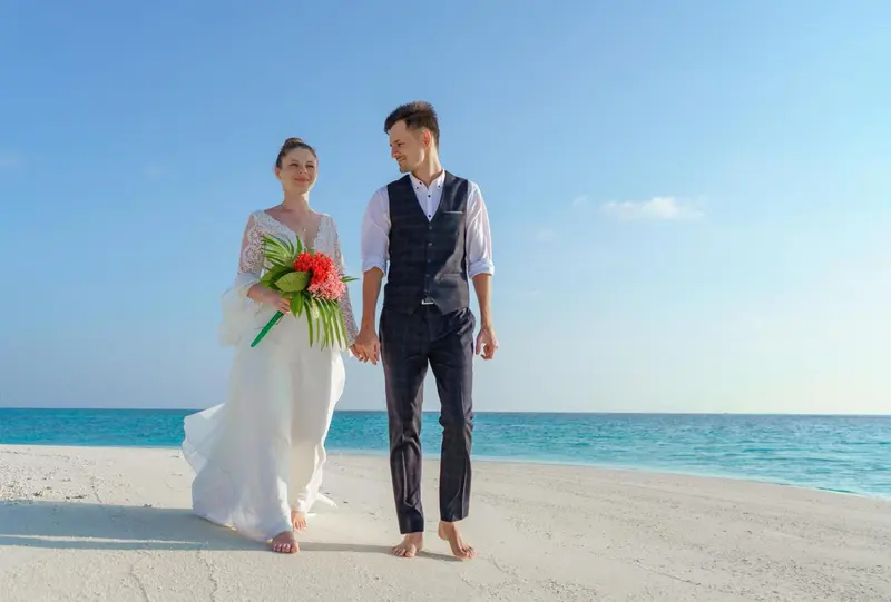 Un couple se promène sur une plage de sable blanc face à la mer.
