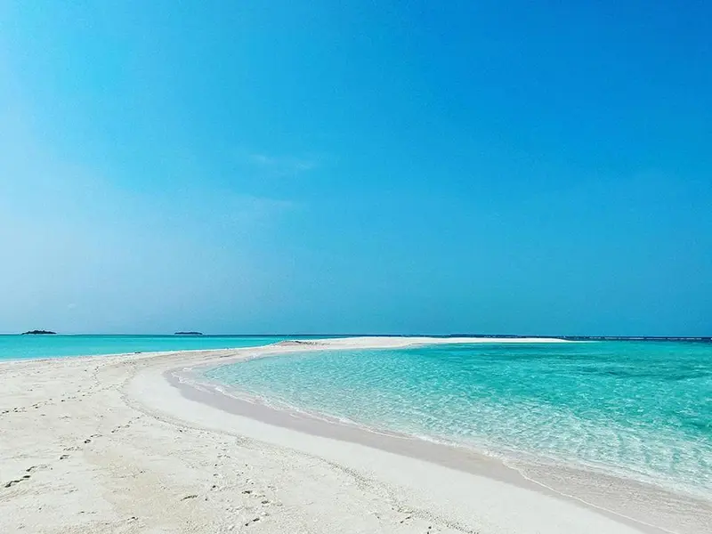 Une étendue de sable blanc bordée par une eau turquoise et un ciel bleu clair.