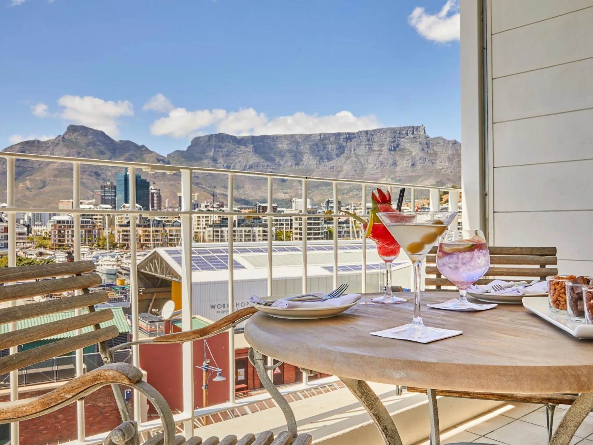 Une table avec des boissons et des amuse-gueules sur une terrasse avec vue sur la ville et les montagnes.