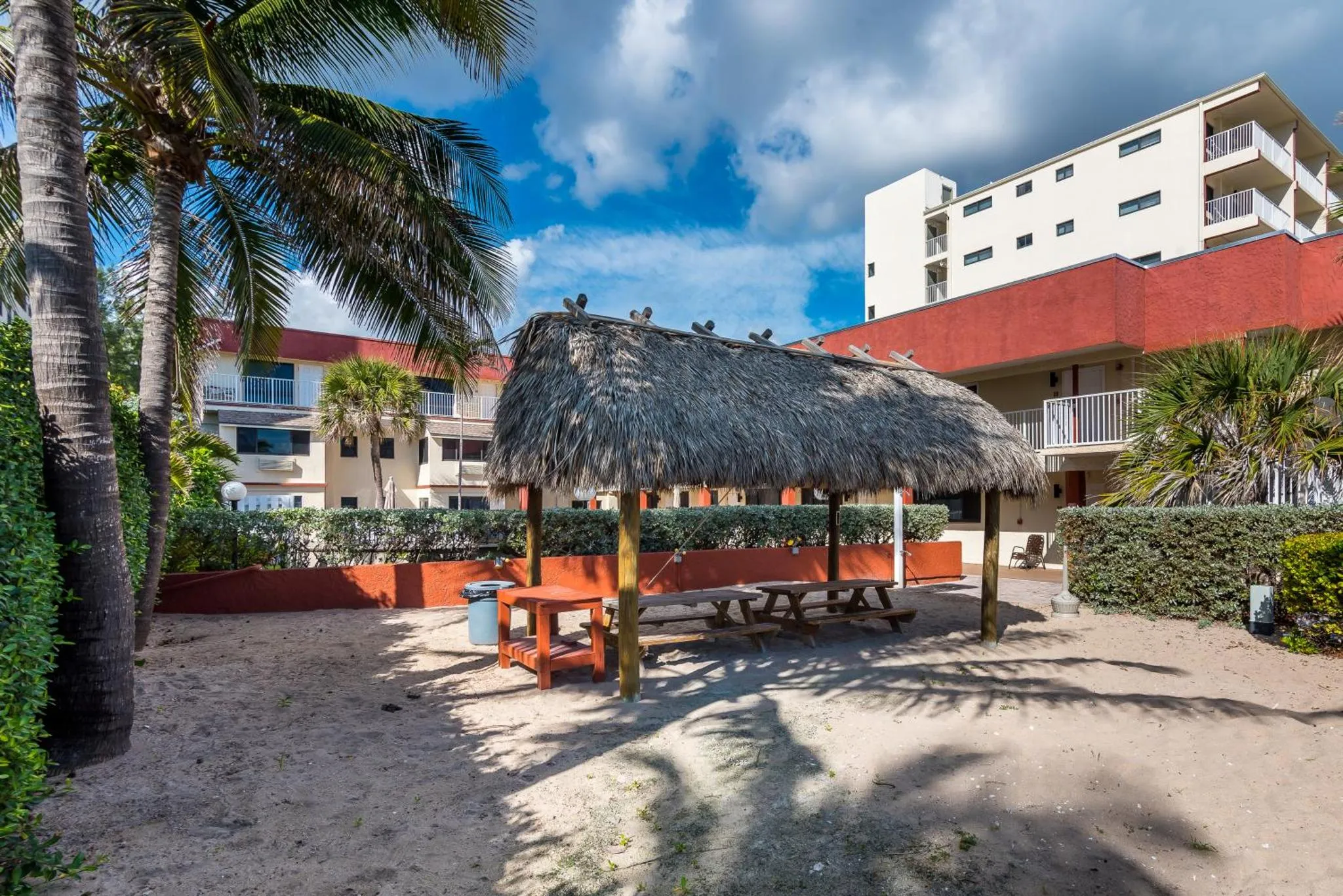 Un abri de plage en chaume offre de l'ombre sur une terrasse sablonneuse.