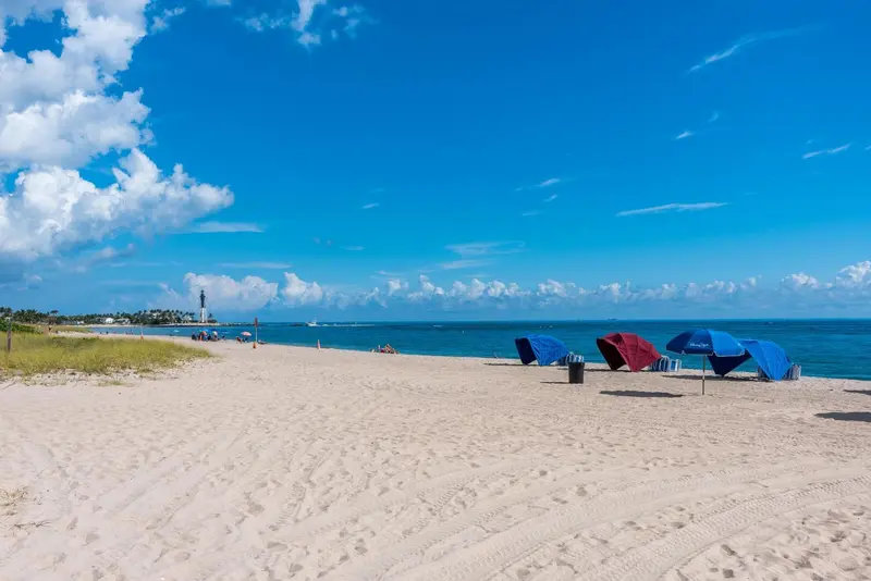 Plage de sable fin avec parasols colorés sous un ciel bleu nuageux.