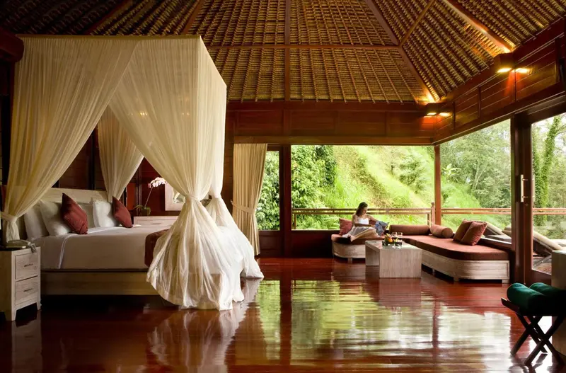 Une chambre spacieuse avec un lit à baldaquin et un coin salon ouvert sur une végétation luxuriante.