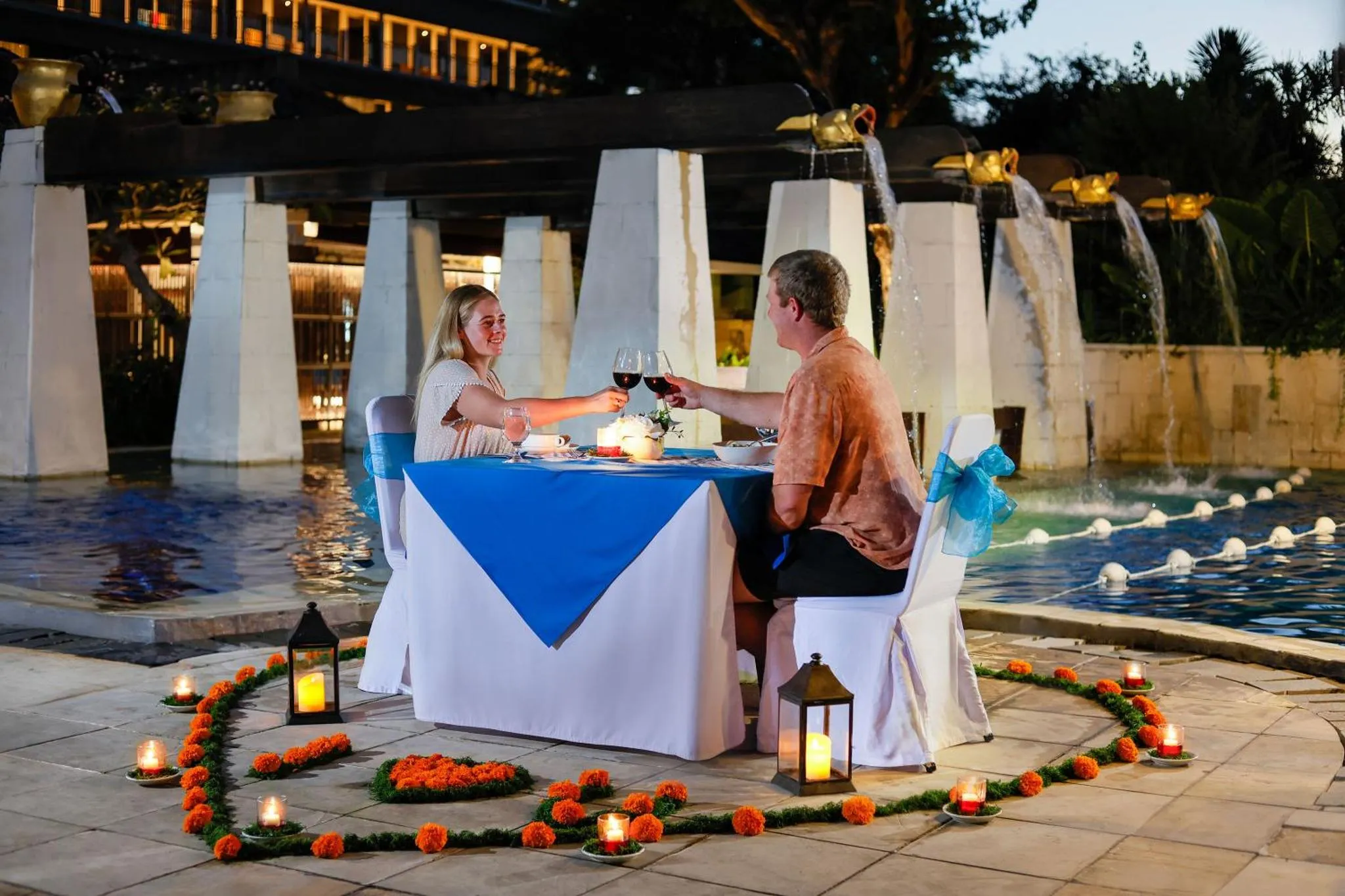Un couple dîne à une table illuminée au bord d'une piscine décorée.