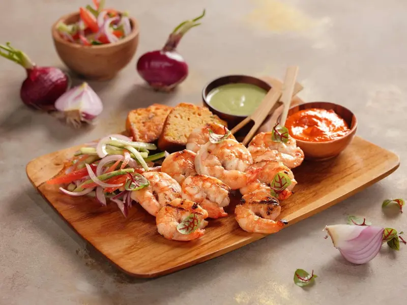 Assiette de crevettes grillées accompagnées de légumes et de sauces.