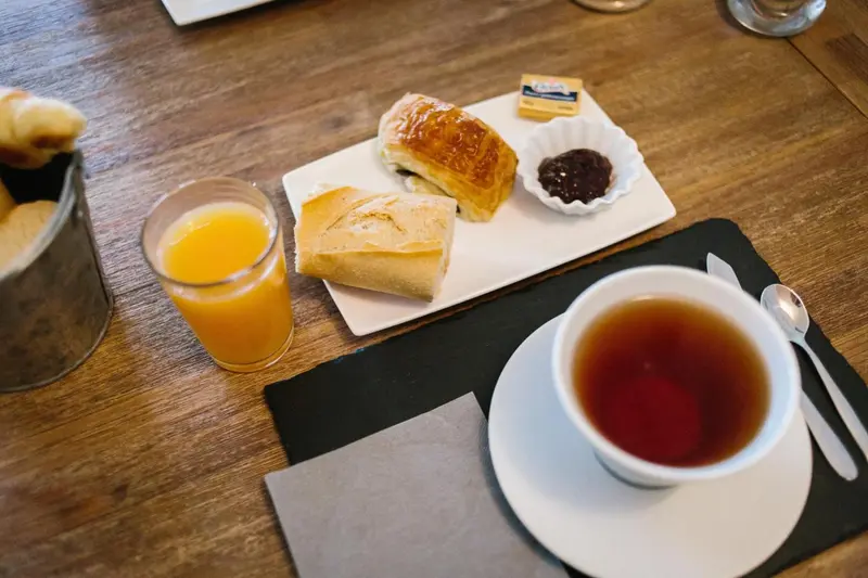 Un petit-déjeuner avec viennoiseries, jus d'orange et boisson chaude est présenté sur une table en bois.