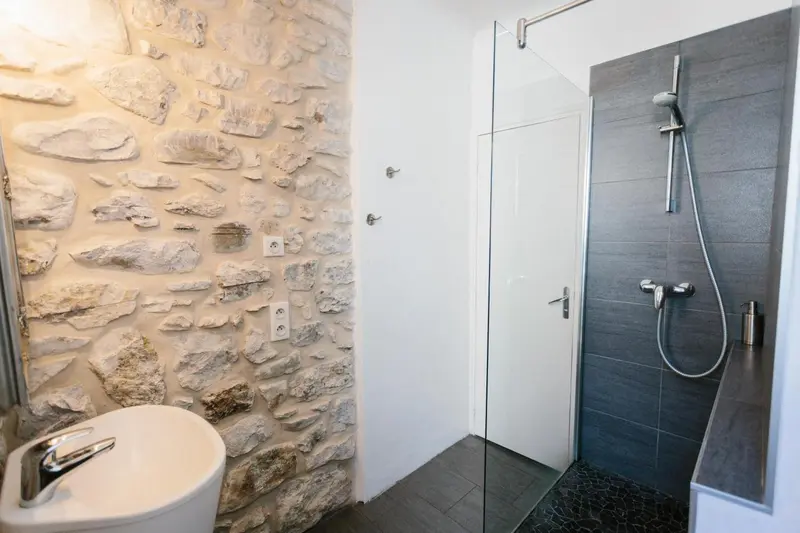 Une salle de bain moderne avec douche à l'italienne et mur en pierre.