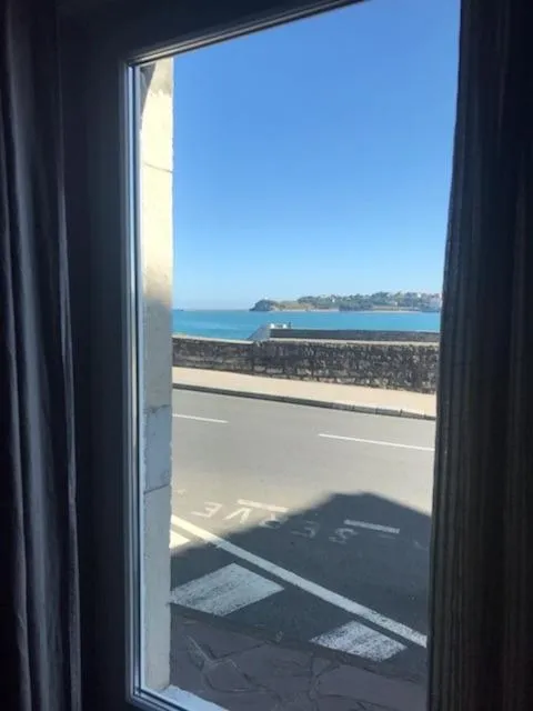 Vue sur la mer depuis une fenêtre avec un rideau.