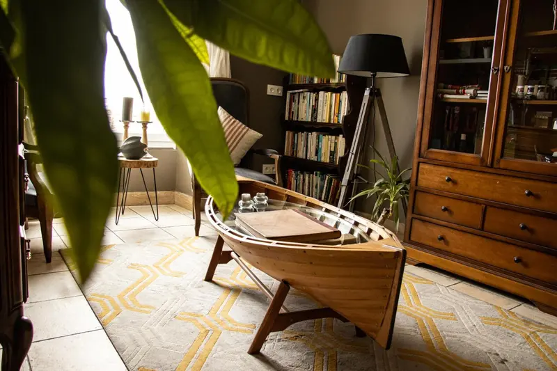 Une table basse originale en forme de coque de bateau se trouve dans un intérieur décoré avec des meubles en bois et des plantes.