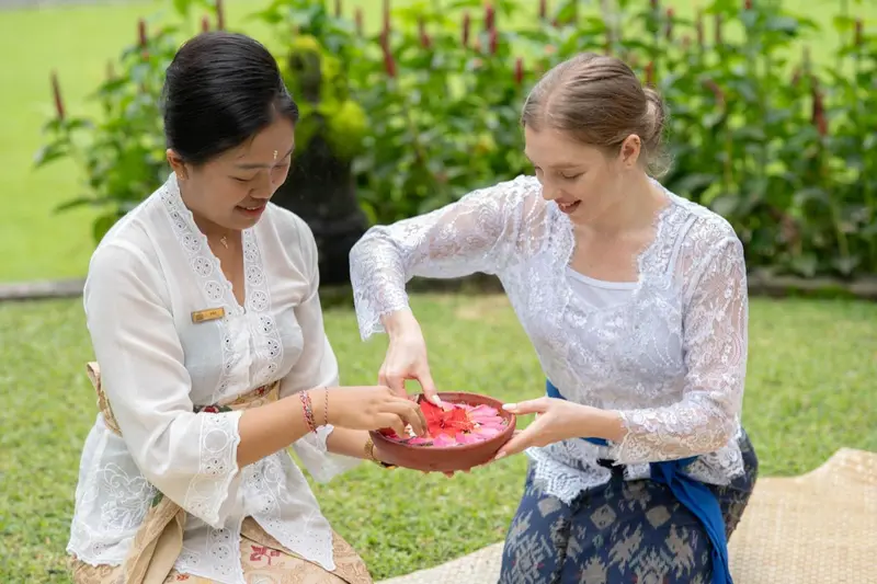 Deux femmes sourient en manipulant des pétales de fleurs dans un jardin.
