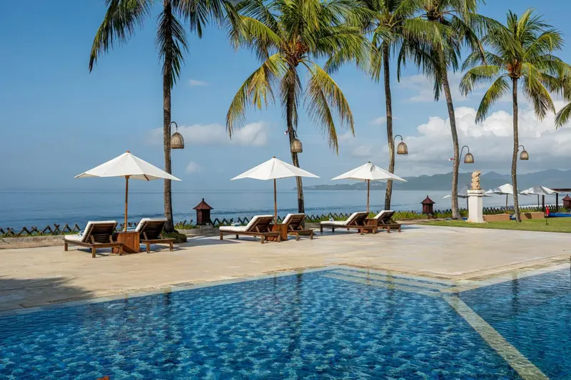 Transats et parasols blancs disposés au bord d'une piscine turquoise, avec des palmiers en arrière-plan.