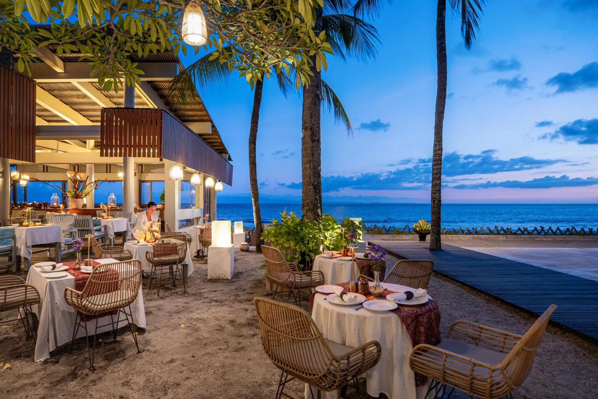 Tables de restaurant en extérieur face à la mer au coucher du soleil.