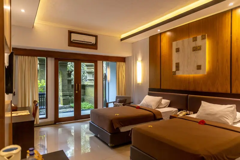 Chambre lumineuse avec deux lits et vue sur une végétation luxuriante.
