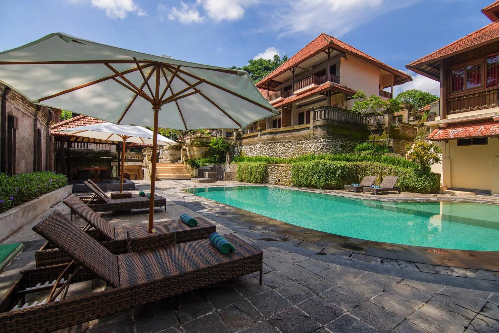 Transats et parasols ombragent une piscine rectangulaire bordée d'une terrasse pavée.