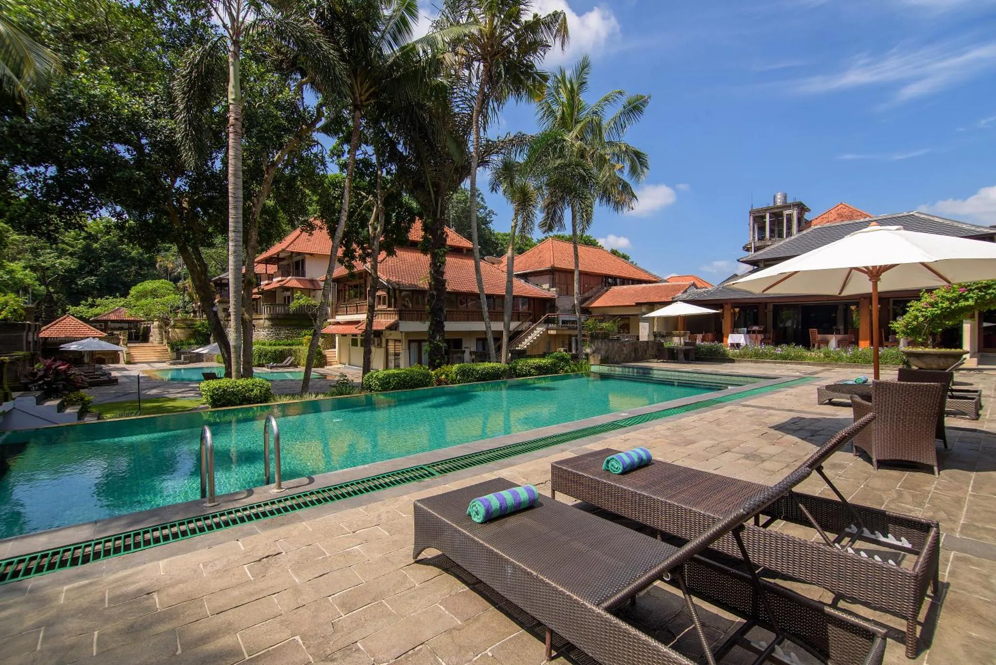 Transats et parasols bordent une piscine turquoise dans un cadre tropical.