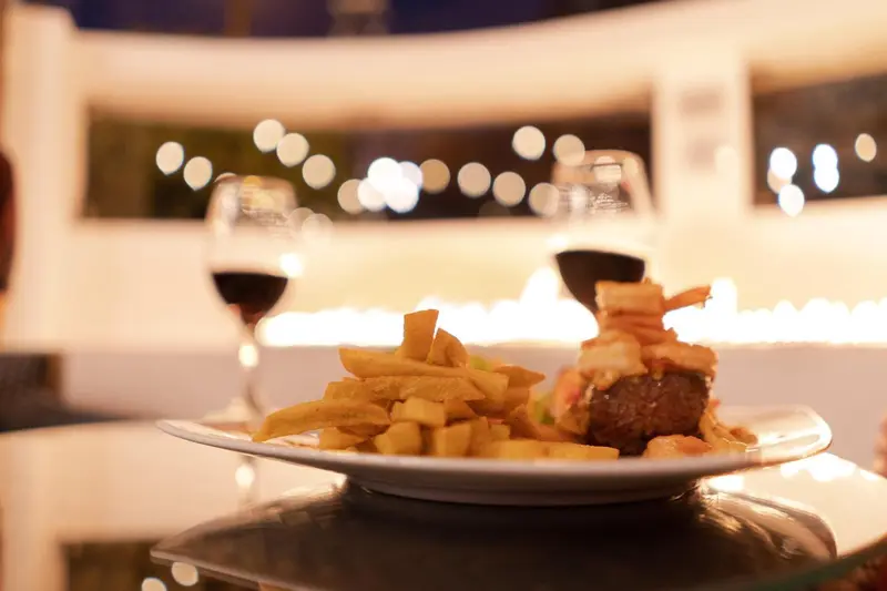 Assiette de frites et de viande avec deux verres de vin sur une table en soirée.
