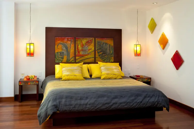 Une chambre lumineuse avec un grand lit décoré de coussins colorés et des tableaux abstraits.
