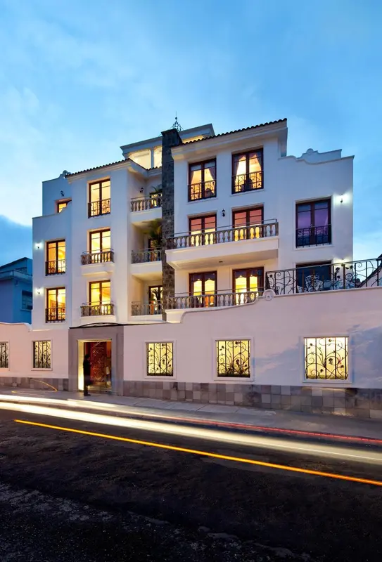 Bâtiment blanc à plusieurs étages illuminé le soir, avec des balcons et des fenêtres.