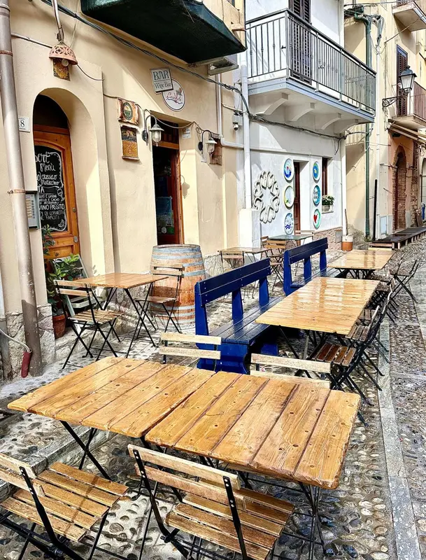 Terrasse de café avec tables en bois et chaises métalliques dans une ruelle pavée.