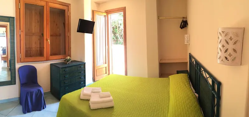 Une chambre lumineuse avec un lit recouvert d'une couverture verte et un meuble en bois.