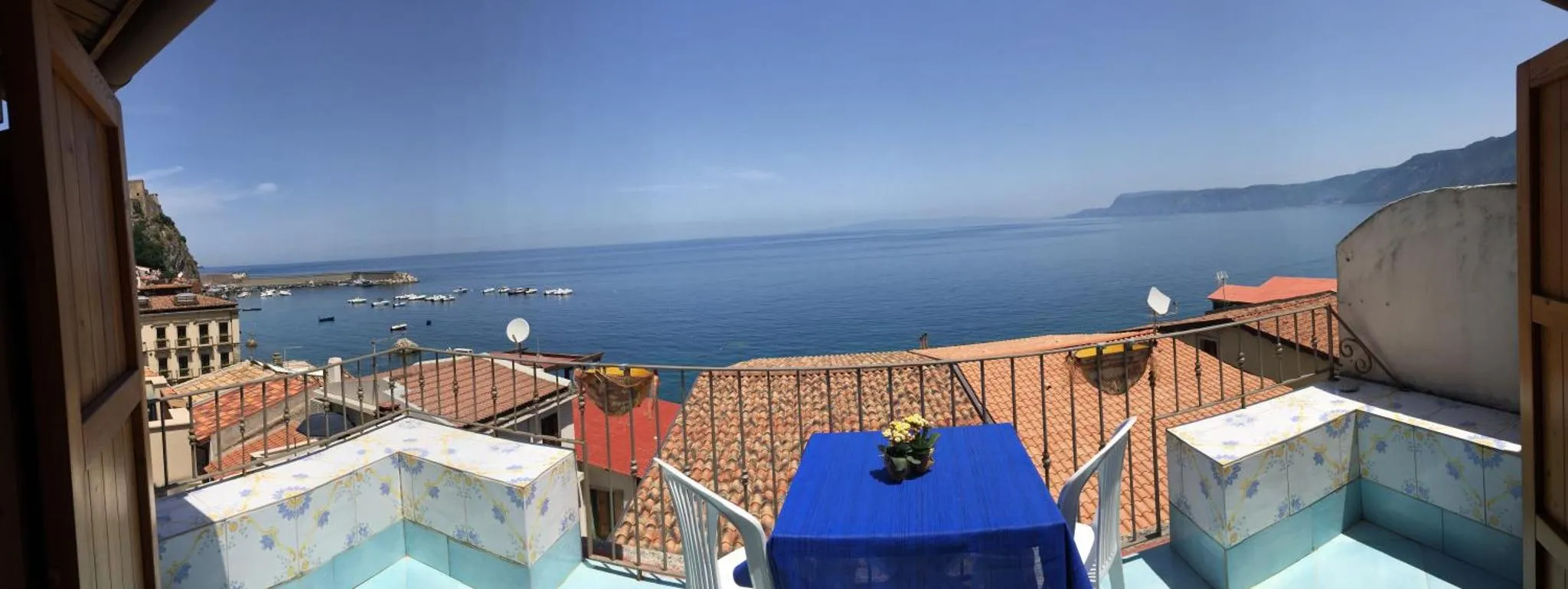 Vue d'une terrasse avec une table bleue donnant sur la mer et les toits d'une ville côtière.