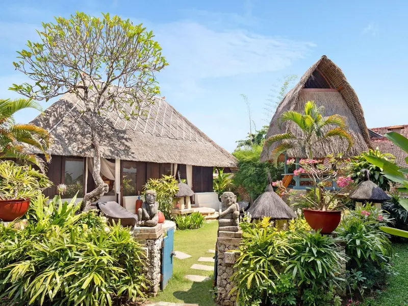 Petites maisons aux toits de chaume dans un jardin tropical luxuriant.