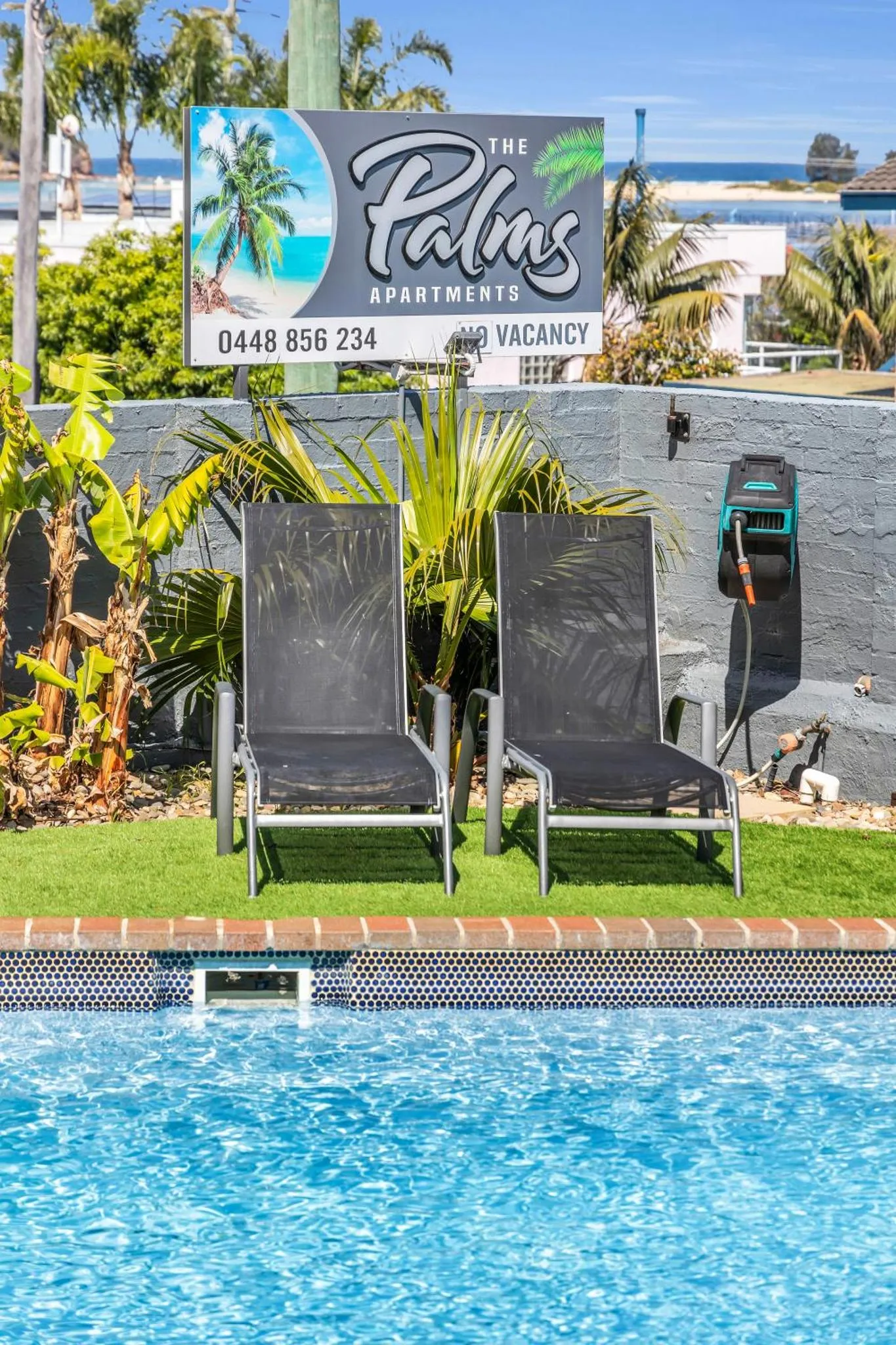 Transats bleus au bord d'une piscine turquoise, devant un bâtiment avec une végétation tropicale.
