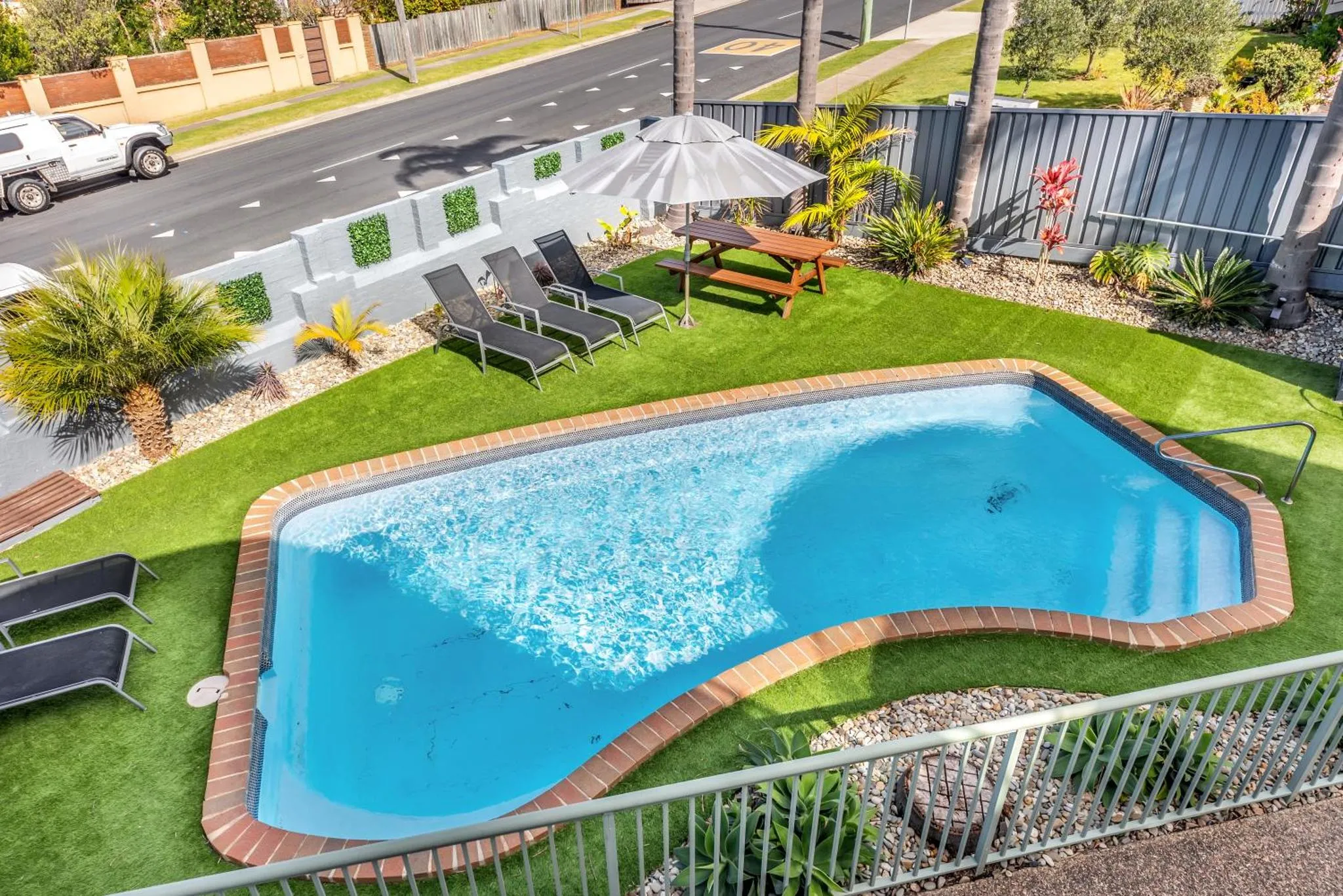 Une piscine rectangulaire avec des transats et des tables de pique-nique dans un jardin soigné.
