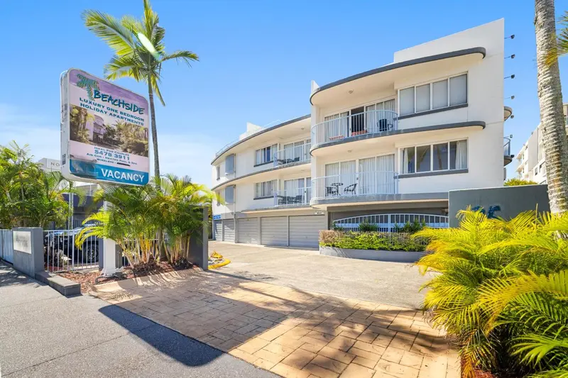Façade d'un immeuble blanc avec des balcons et une végétation tropicale.