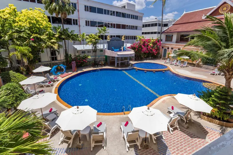 Vue aérienne d'une piscine entourée de transats et de parasols, avec un bâtiment en arrière-plan.