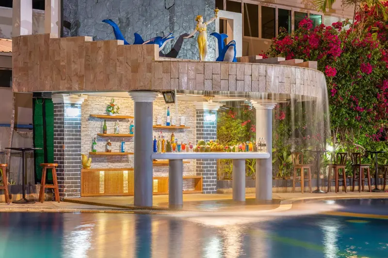 Un bar illuminé avec des tabourets et une cascade d'eau en arrière-plan.