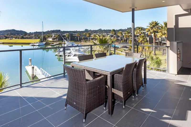 Une table à manger en rotin sur une terrasse carrelée avec vue sur un port de plaisance.