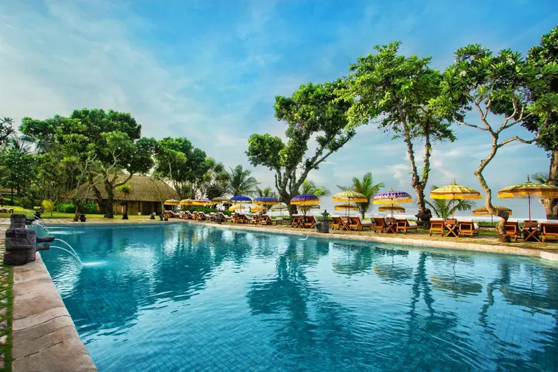 Une piscine turquoise bordée de transats sous des parasols colorés, avec une végétation luxuriante en arrière-plan.