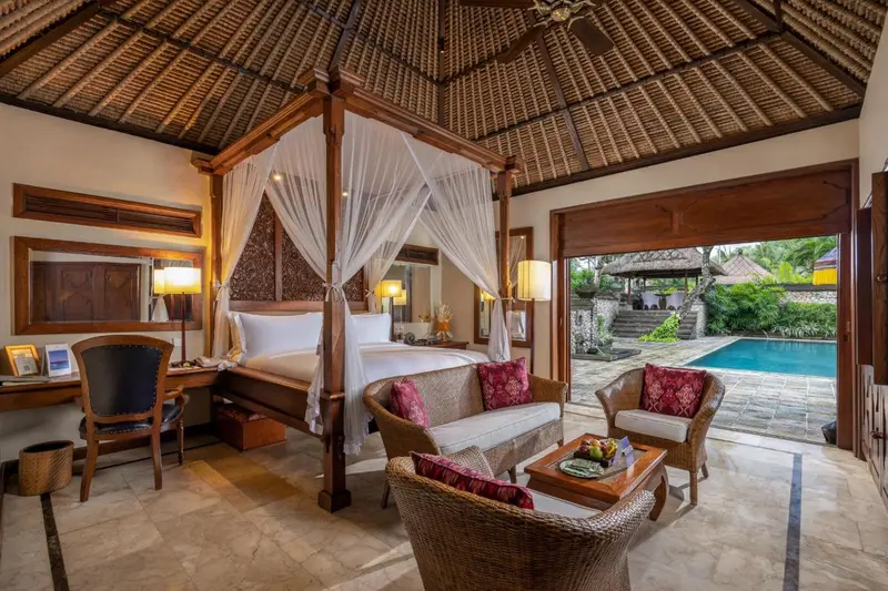 Une chambre avec un grand lit à baldaquin et un coin salon donnant sur une piscine.