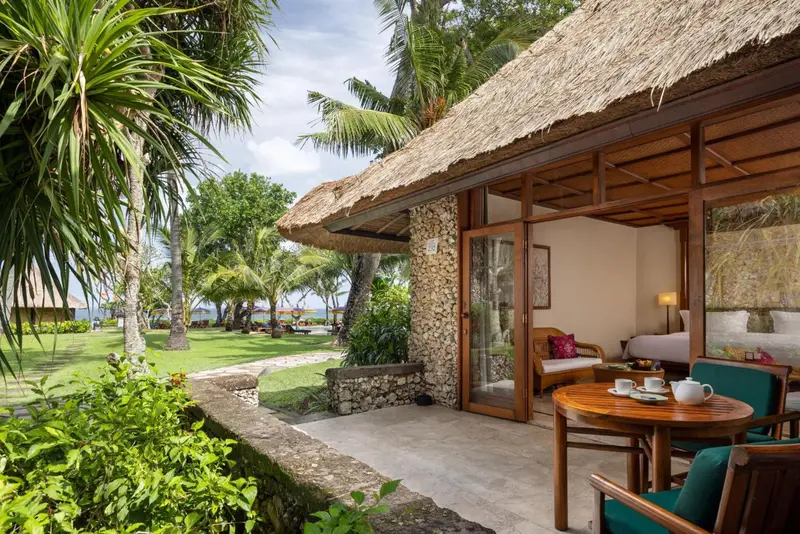 Une terrasse ombragée donne sur un jardin verdoyant et une plage.