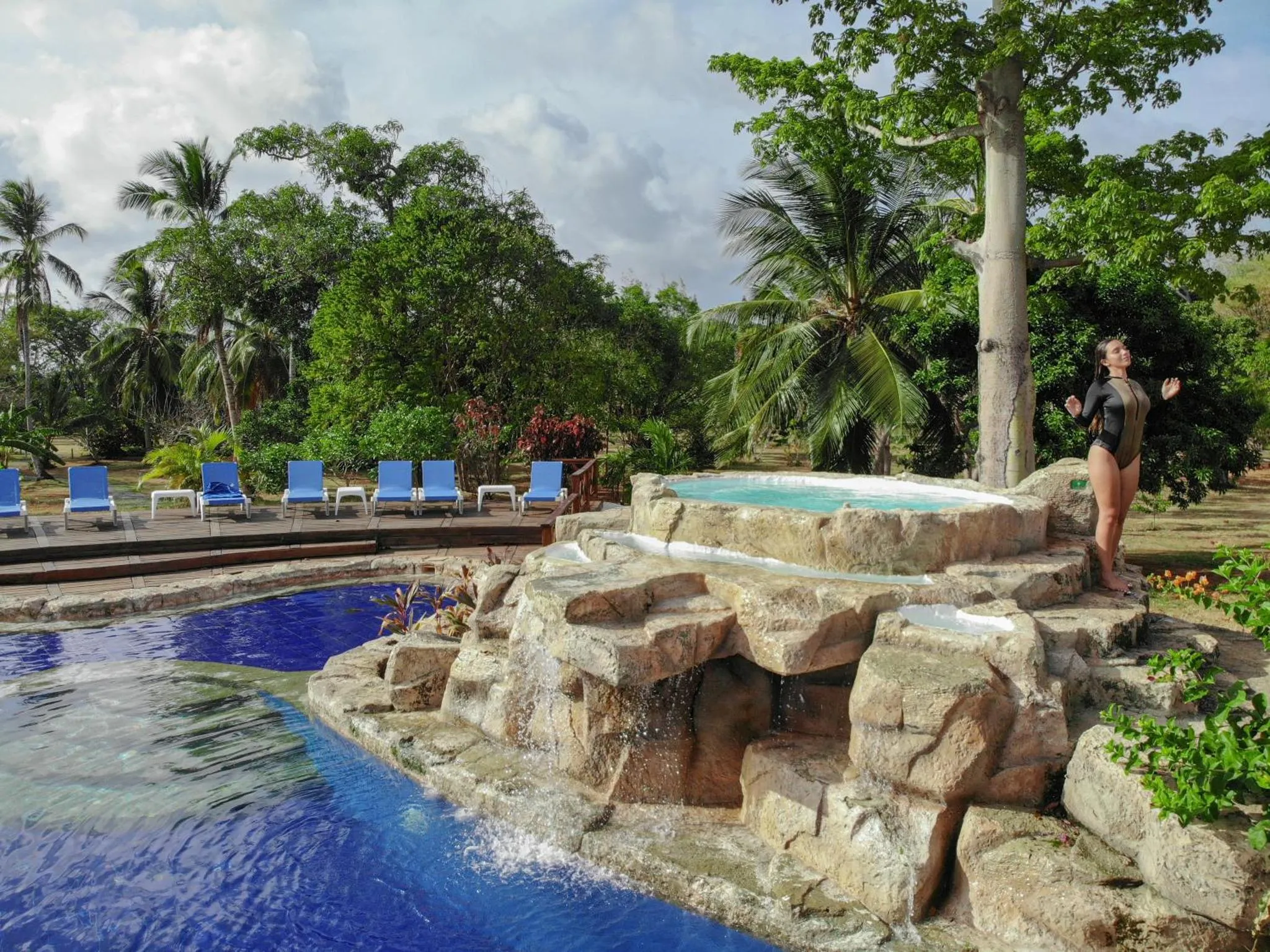 Une piscine avec une cascade rocheuse et des transats sur une terrasse.