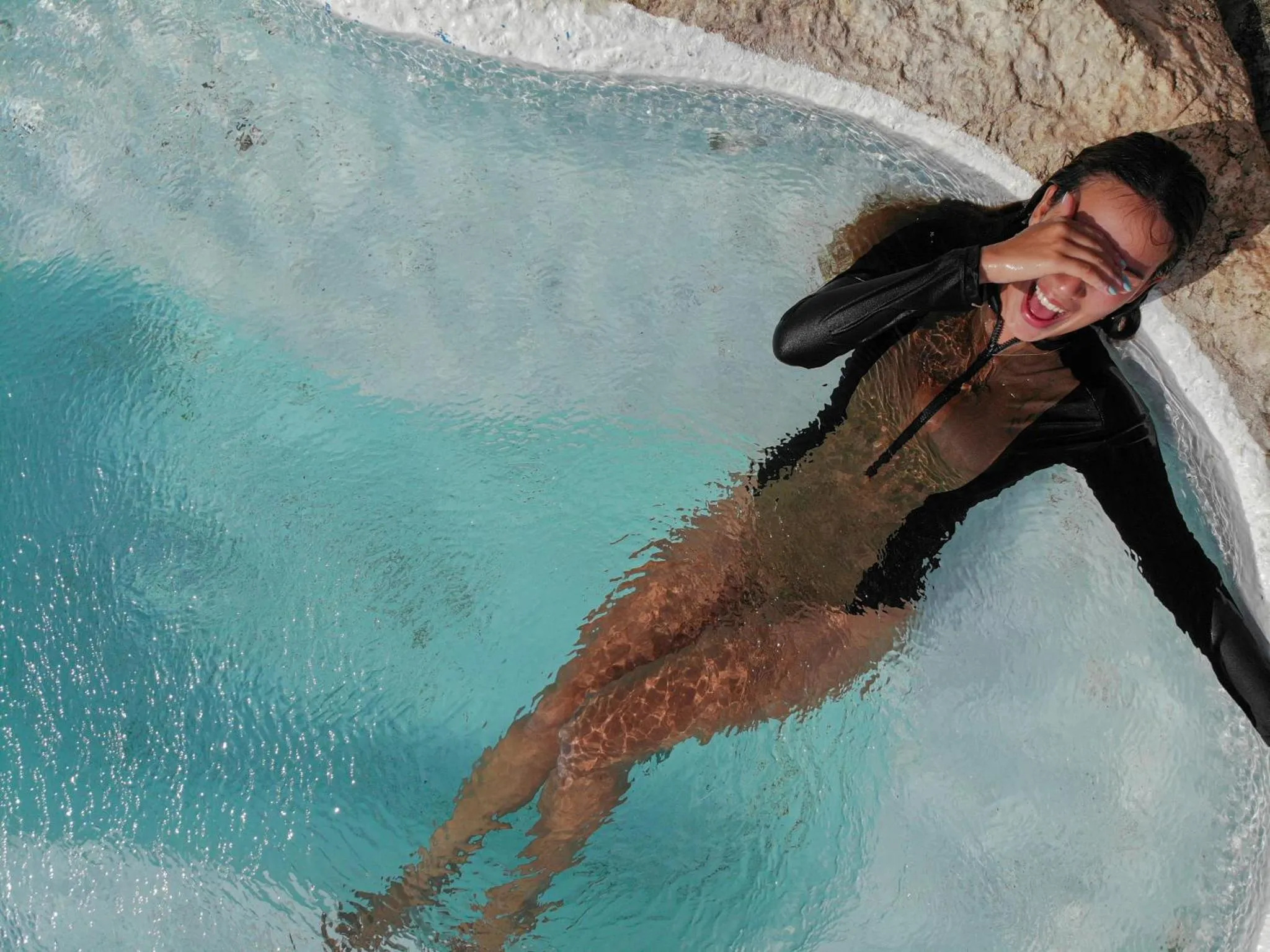 Une personne souriante flotte dans une piscine turquoise.
