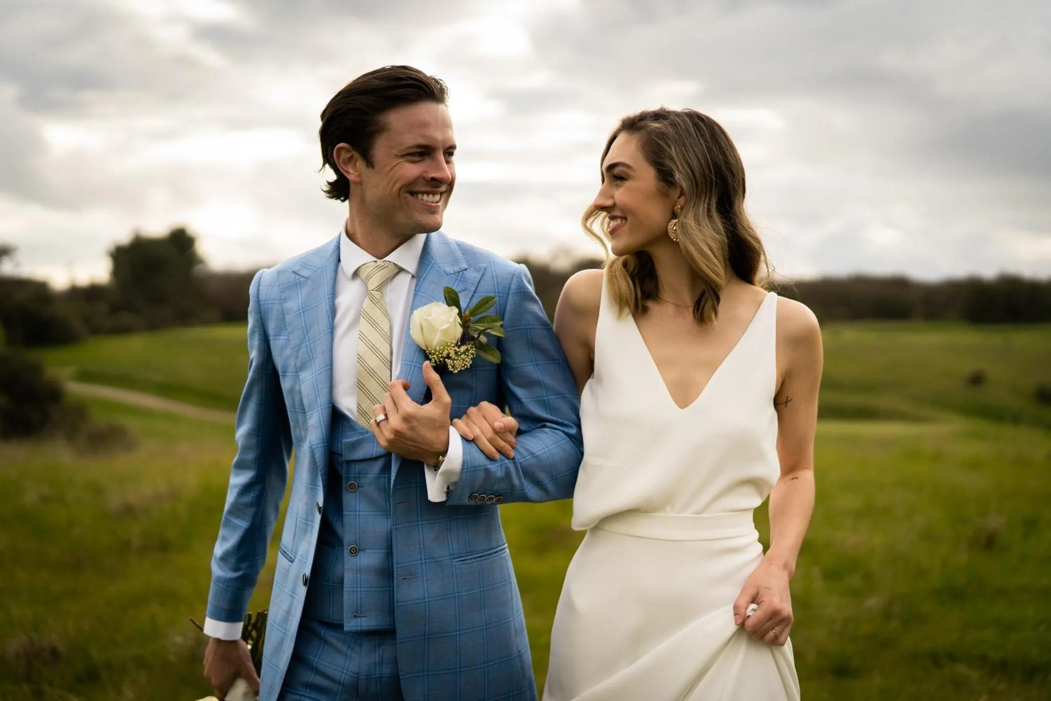 Un couple souriant se promène dans un paysage verdoyant.
