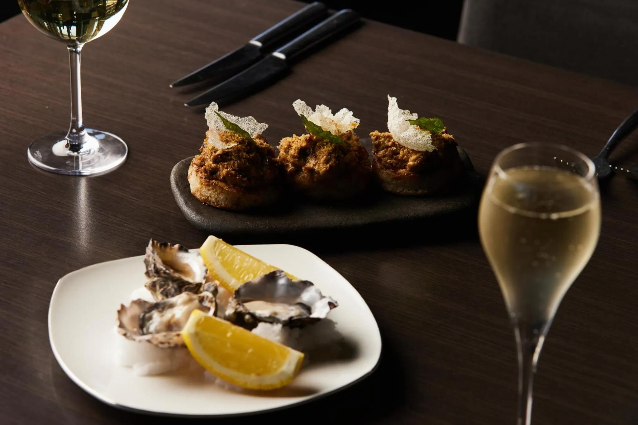 Assiettes de fruits de mer et verres de vin sur une table sombre.