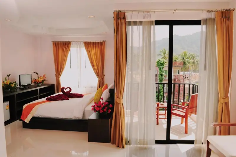 Une chambre lumineuse avec un lit decoré et un balcon donnant sur un paysage montagneux.