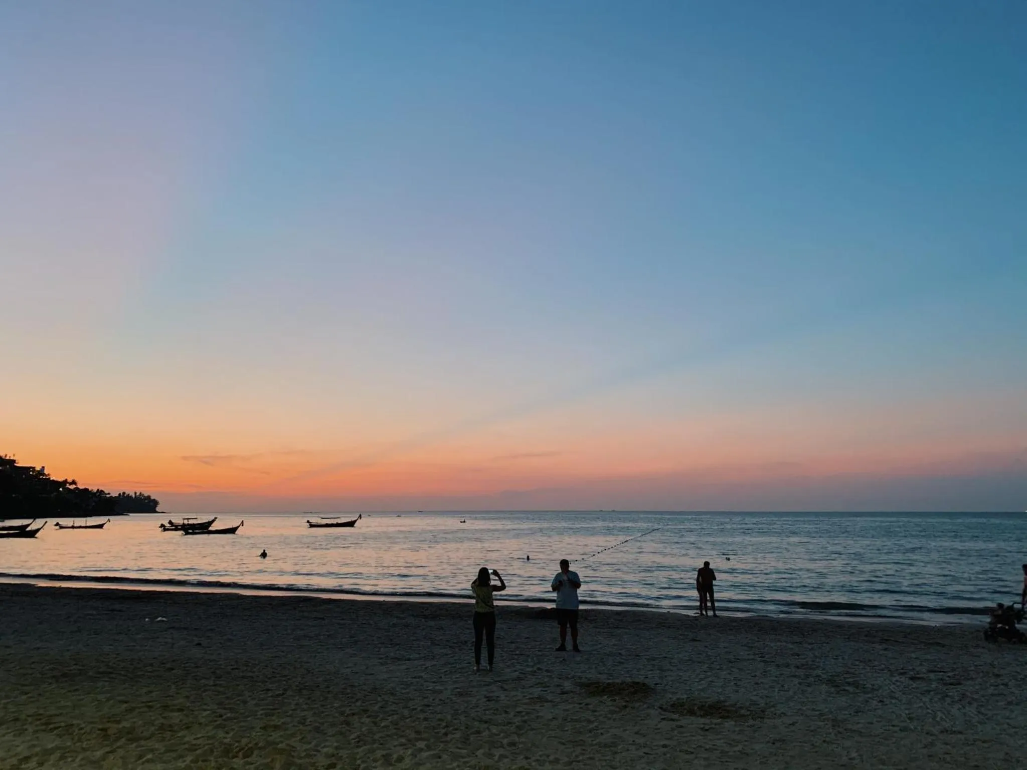 Des personnes se promènent sur une plage au coucher du soleil.