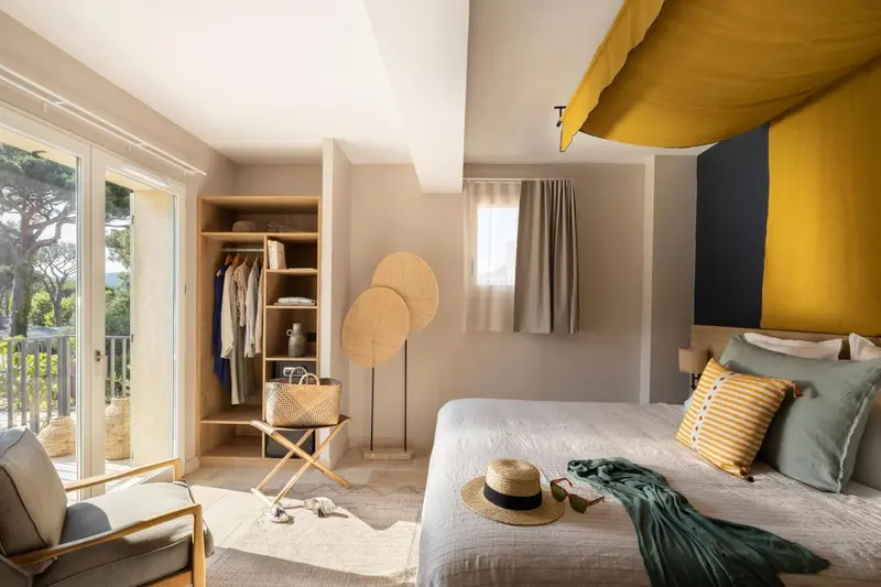 Une chambre lumineuse avec un lit recouvert d'un couvre-lit blanc et de coussins colorés.