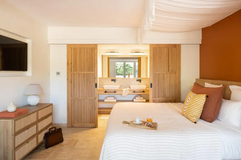 Une chambre lumineuse avec un lit fait et une salle de bain visible au fond.